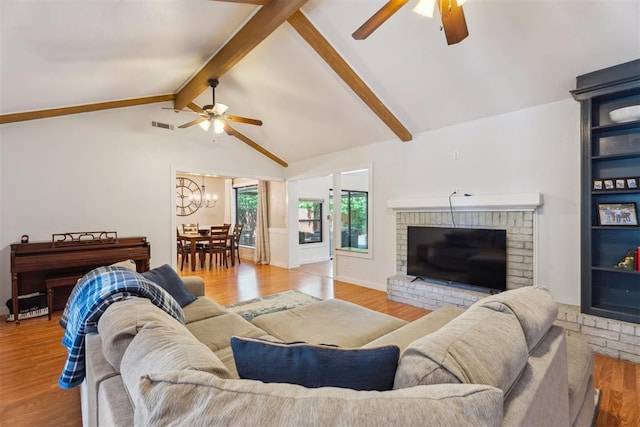 living room with ceiling fan, wood finished floors, a chandelier, and a brick fireplace