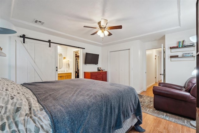 bedroom featuring light wood-style flooring, a barn door, a closet, a ceiling fan, and connected bathroom
