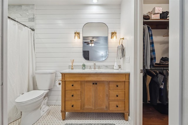 bathroom with toilet, ceiling fan, vanity, a spacious closet, and wood walls