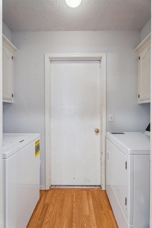 laundry area with cabinet space, washing machine and clothes dryer, light wood-style floors, and a textured ceiling