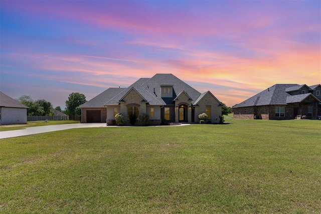 french provincial home featuring concrete driveway, an attached garage, stone siding, and a yard