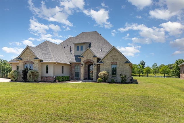 french country style house featuring stone siding, a front lawn, stucco siding, and roof with shingles