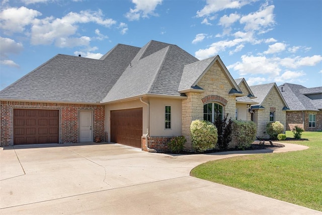 french country inspired facade featuring a garage, driveway, a shingled roof, a front lawn, and stone siding