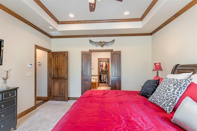 carpeted bedroom with a tray ceiling, ornamental molding, a walk in closet, baseboards, and a ceiling fan