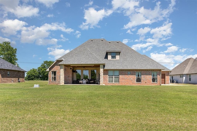 back of property with brick siding, a shingled roof, a yard, and a patio area