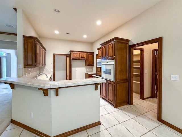 3424 Teton Ct, Norman, OK 73072 - kitchen featuring white appliances, a peninsula, a breakfast bar area, tasteful backsplash, and baseboards