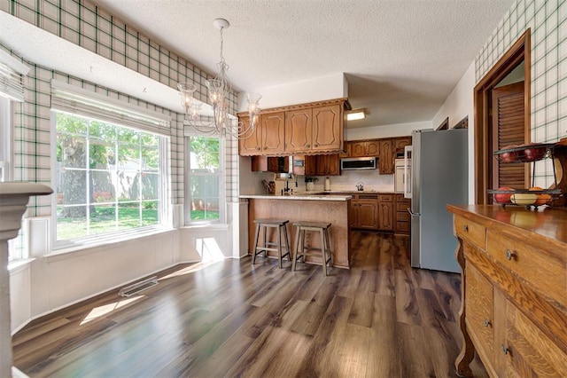 5708 NW 87th St, Oklahoma City, OK 73132 - kitchen with appliances with stainless steel finishes, a textured ceiling, a peninsula, dark wood finished floors, and light countertops
