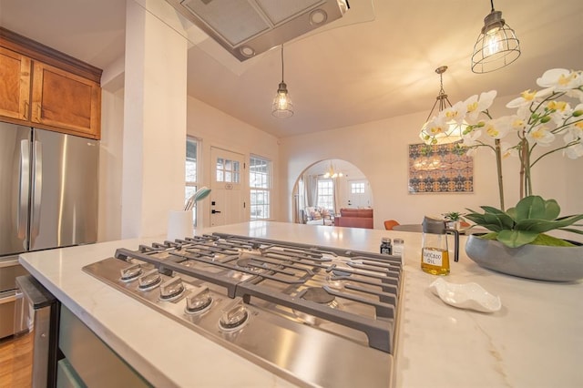1017 Dean Pl, Oklahoma City, OK 73117 - kitchen with brown cabinets, stainless steel appliances, hanging light fixtures, arched walkways, and light stone counters