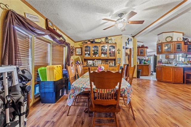 dining area with lofted ceiling, a textured ceiling, light wood-style flooring, ornamental molding, and a ceiling fan