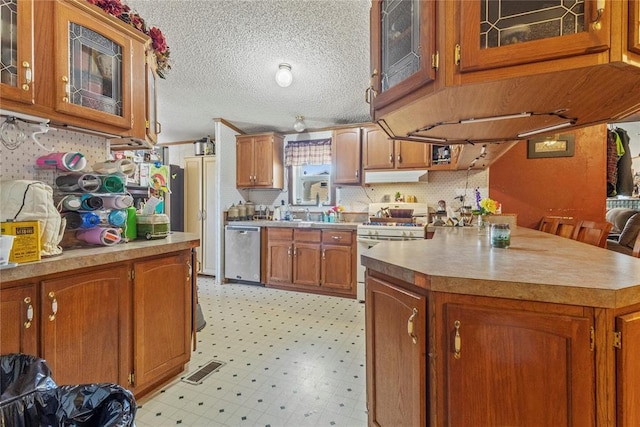 kitchen featuring dishwasher, gas range gas stove, under cabinet range hood, brown cabinetry, and light floors