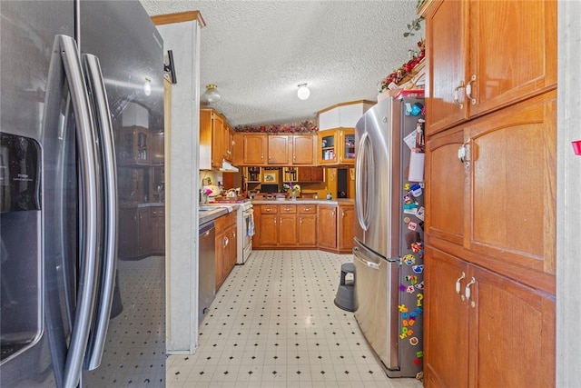 kitchen with appliances with stainless steel finishes, light floors, brown cabinetry, light countertops, and a textured ceiling