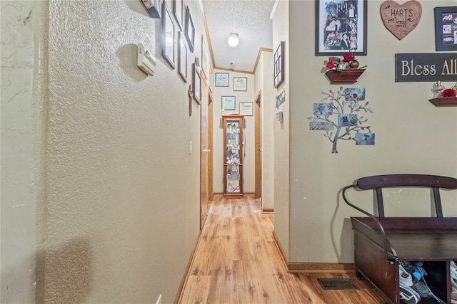 corridor with light wood finished floors, baseboards, and a textured wall