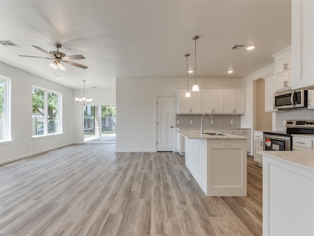 kitchen with appliances with stainless steel finishes, light countertops, a sink, a ceiling fan, and light wood finished floors