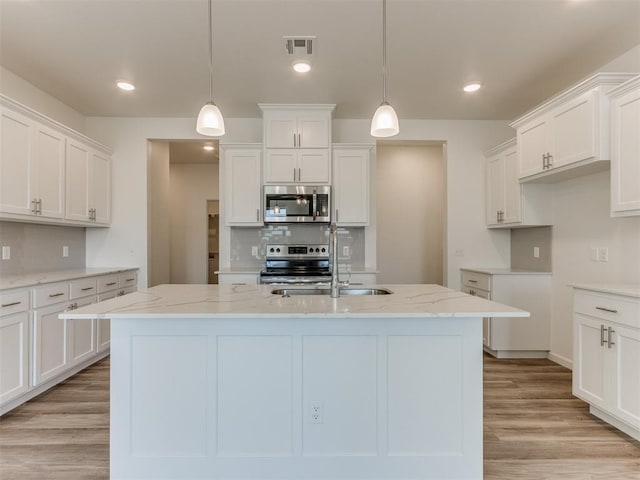 kitchen featuring stainless steel appliances, light stone countertops, a sink, an island with sink, and decorative backsplash