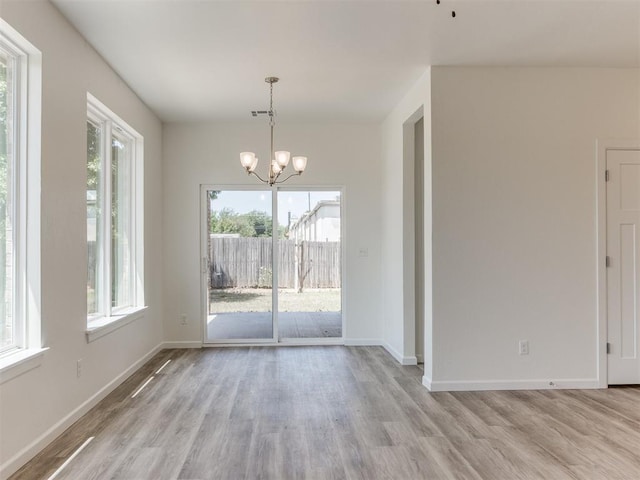 unfurnished dining area with light wood-type flooring, a chandelier, and plenty of natural light