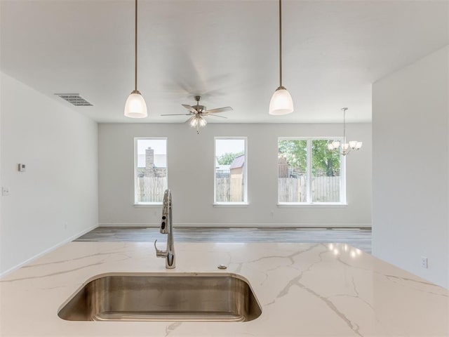 kitchen with a sink, healthy amount of natural light, light stone countertops, and pendant lighting