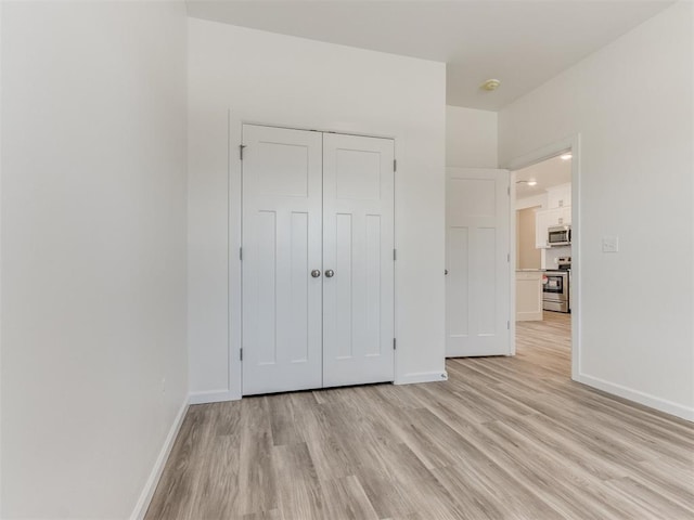 unfurnished bedroom featuring light wood-type flooring, baseboards, and a closet