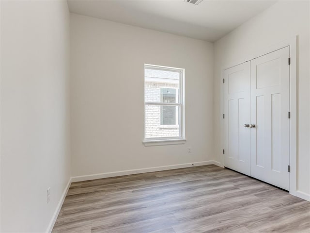 unfurnished bedroom with light wood-style flooring, baseboards, and a closet