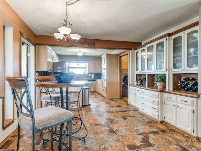 13776 E Stella Rd, Newalla, OK 74857 - kitchen featuring washer / clothes dryer, a textured ceiling, glass insert cabinets, a chandelier, and appliances with stainless steel finishes