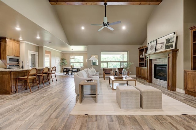 12535 Memory Ln, Edmond, OK 73025 - living area featuring high vaulted ceiling, a tiled fireplace, ceiling fan, light wood finished floors, and baseboards