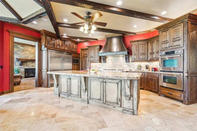 13600 W Britton Rd, Yukon, OK 73099 - kitchen featuring built in appliances, premium range hood, stone tile flooring, backsplash, and beam ceiling