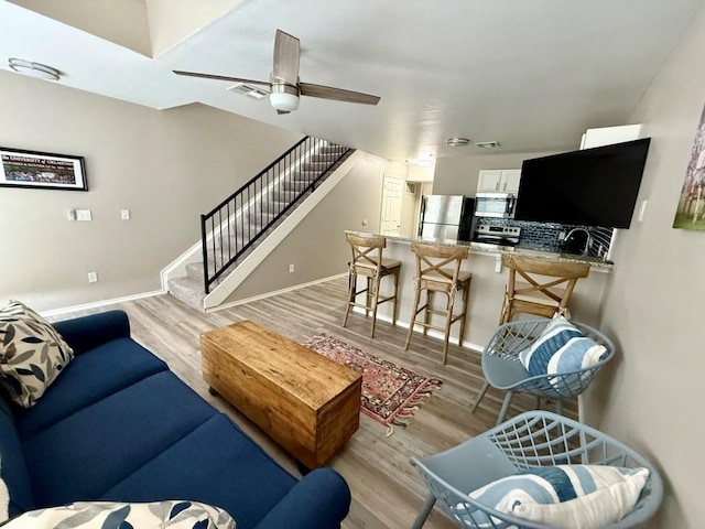 living room with stairs, light wood-style floors, baseboards, and ceiling fan