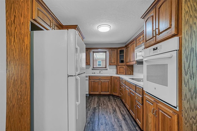 kitchen with white appliances, a textured ceiling, dark wood-style floors, brown cabinetry, and a sink