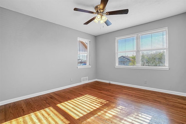 unfurnished room featuring healthy amount of natural light, baseboards, wood finished floors, and a ceiling fan