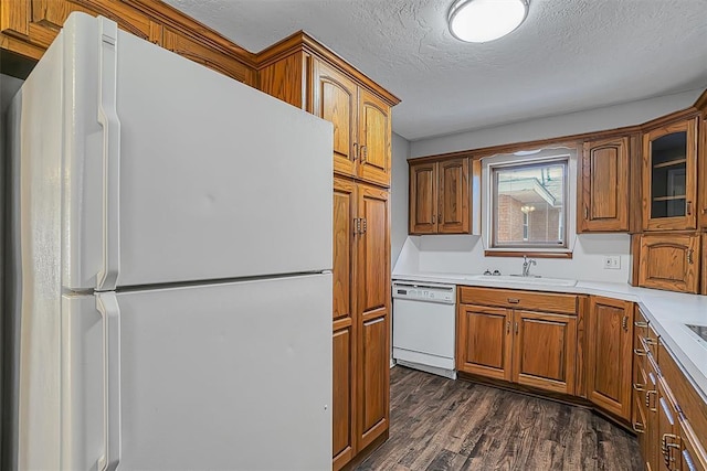 kitchen with white appliances, a sink, brown cabinetry, dark wood-type flooring, and a textured ceiling