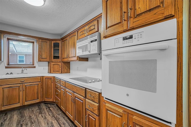 kitchen featuring white appliances, brown cabinets, a textured ceiling, a sink, and dark wood-style floors