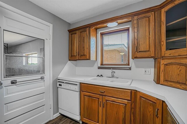 kitchen featuring white dishwasher, a sink, brown cabinetry, and light countertops
