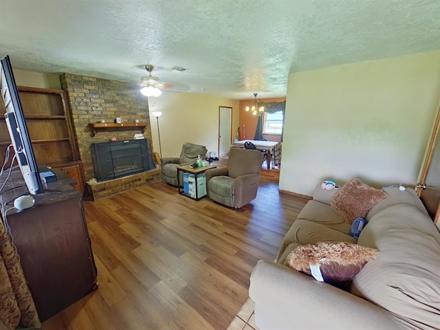 2317 County Road 1268, Blanchard, OK 73010 - living room with a textured ceiling, a brick fireplace, wood finished floors, a chandelier, and a ceiling fan