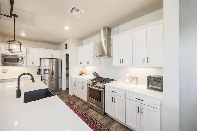 kitchen featuring appliances with stainless steel finishes, wall chimney range hood, a sink, dark wood-style floors, and white cabinetry