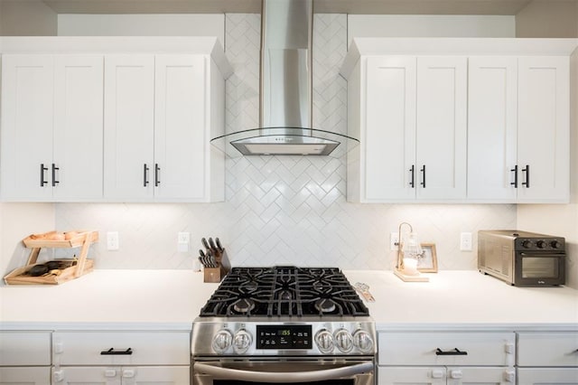 kitchen featuring wall chimney range hood, stainless steel gas range, light countertops, and backsplash