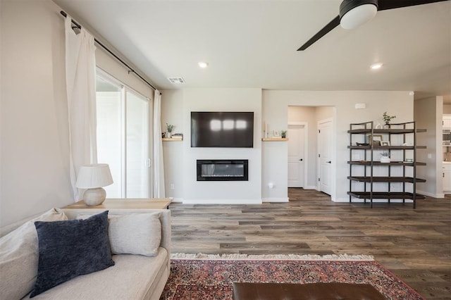 living room featuring a glass covered fireplace, wood finished floors, a ceiling fan, recessed lighting, and baseboards