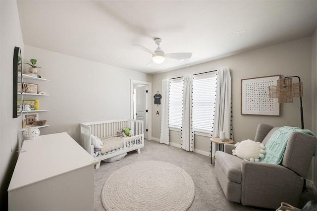 carpeted bedroom with baseboards, a nursery area, and a ceiling fan