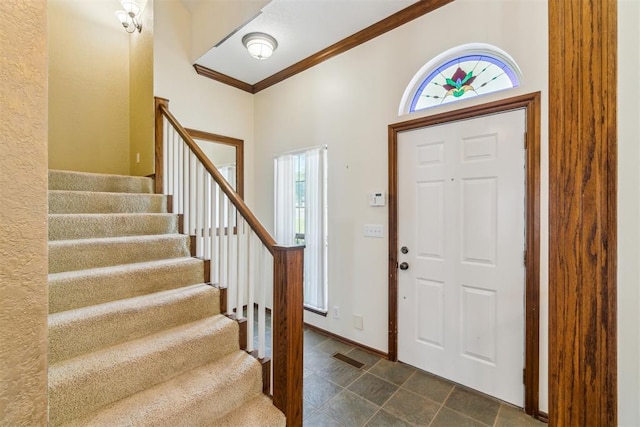 entryway with stairs, crown molding, dark tile patterned floors, and baseboards