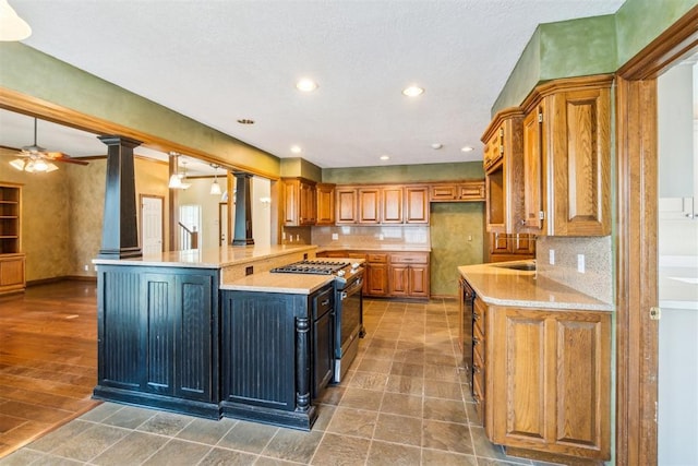 kitchen featuring stainless steel gas range, brown cabinets, backsplash, a ceiling fan, and recessed lighting