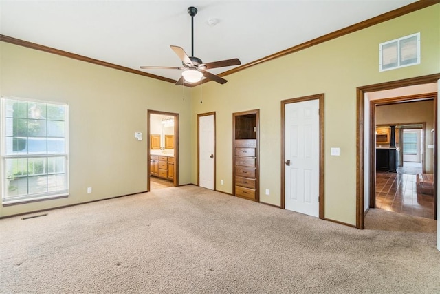 unfurnished bedroom featuring light colored carpet, crown molding, baseboards, connected bathroom, and a ceiling fan