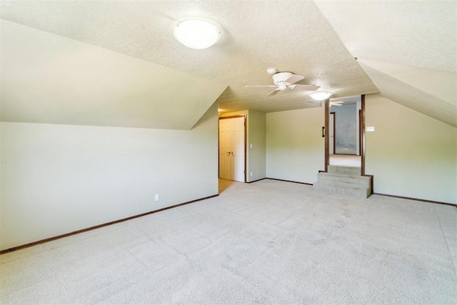 bonus room featuring vaulted ceiling, light carpet, baseboards, a textured ceiling, and a ceiling fan