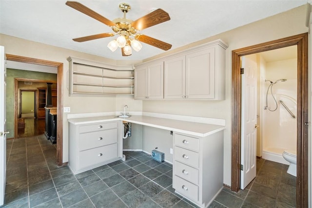 unfurnished office with ceiling fan, built in study area, baseboards, and dark stone finish floors