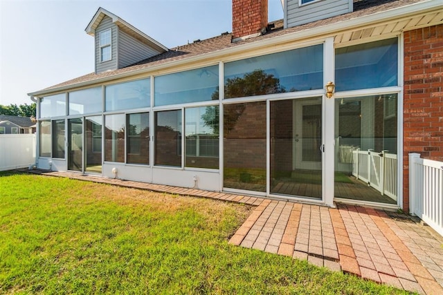 back of property featuring a chimney, a lawn, roof with shingles, a sunroom, and brick siding