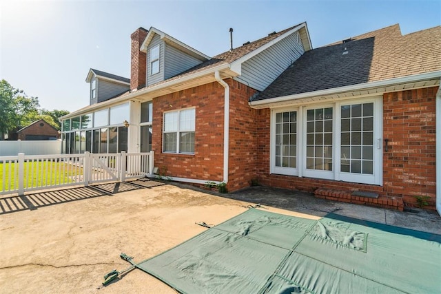 rear view of property with brick siding, a patio, a chimney, and fence