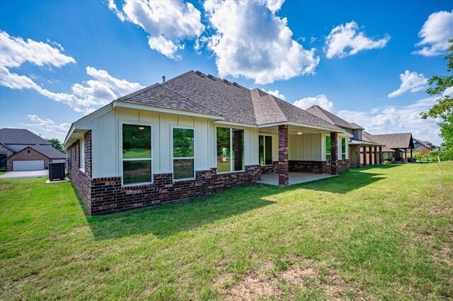 941 Siena Springs Dr, Norman, OK 73071 - rear view of house featuring brick siding, board and batten siding, roof with shingles, central AC, and a yard