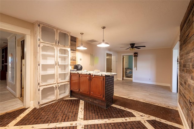 kitchen featuring brown cabinets, ceiling fan, light countertops, baseboards, and hanging light fixtures