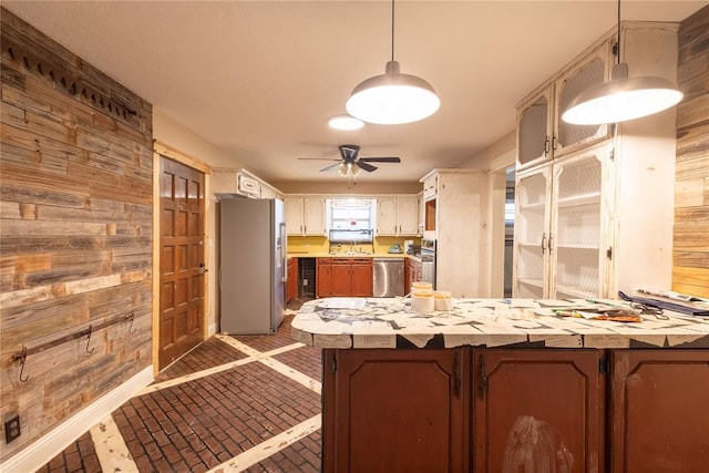 kitchen featuring freestanding refrigerator, stainless steel dishwasher, wooden walls, light countertops, and brick patterned floors
