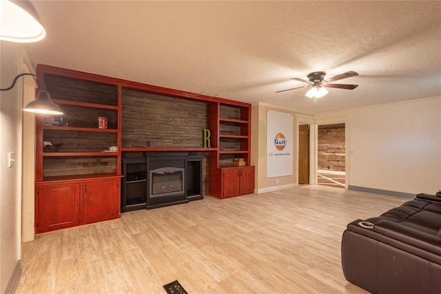 living room with a glass covered fireplace, light wood finished floors, a ceiling fan, baseboards, and a textured ceiling