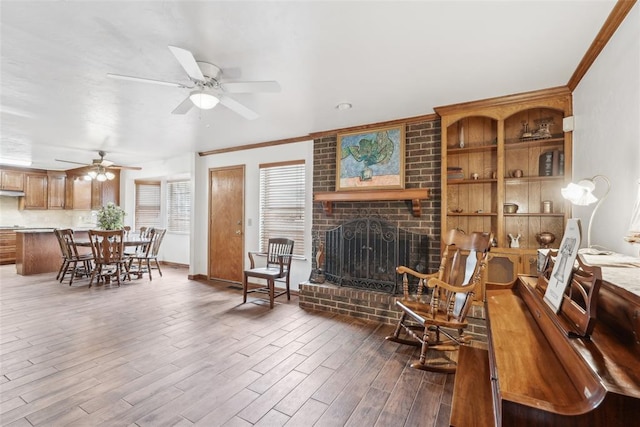 living area with ornamental molding, ceiling fan, wood finished floors, and a brick fireplace