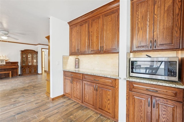 kitchen featuring stainless steel microwave, tasteful backsplash, wood finished floors, ceiling fan, and brown cabinetry