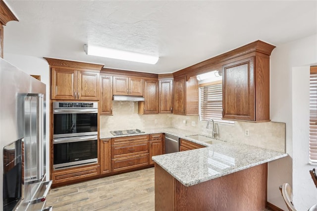 kitchen with appliances with stainless steel finishes, a sink, under cabinet range hood, a peninsula, and brown cabinets